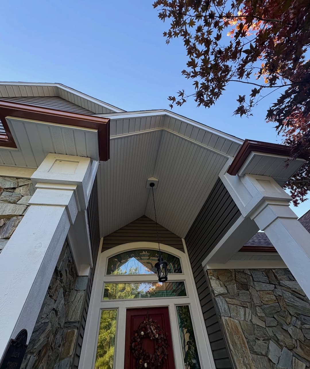 Modern stone and wood entryway with red door and autumn leaves overhead.
