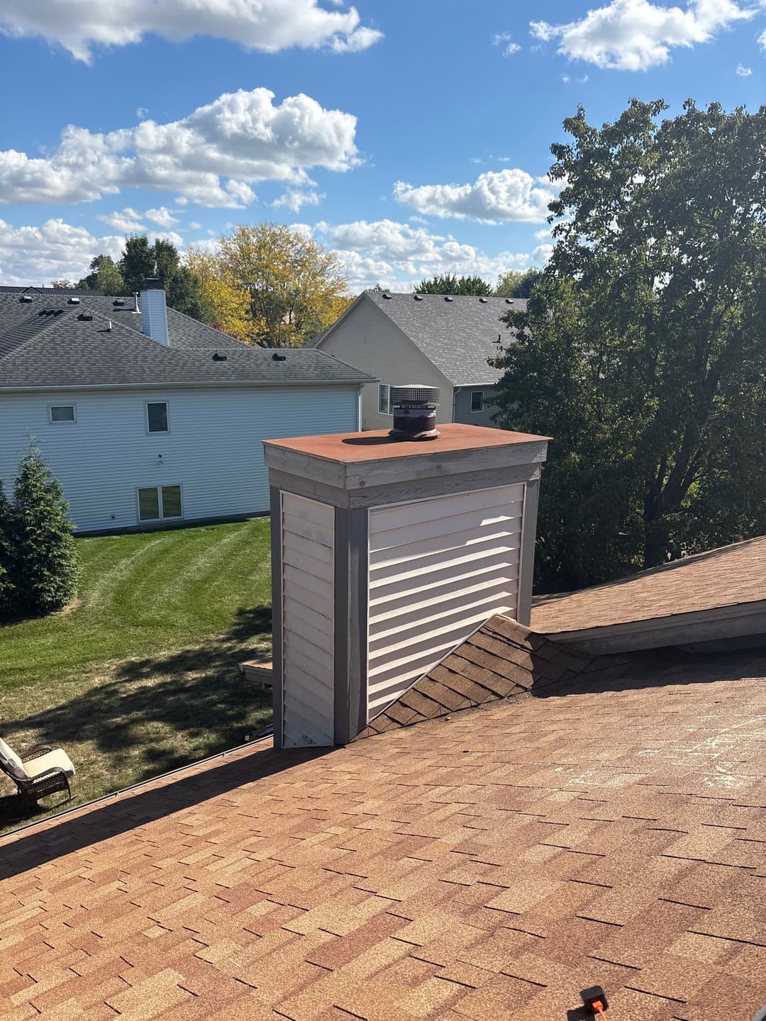 Chimney on a sloped roof with surrounding residential landscape and blue sky.