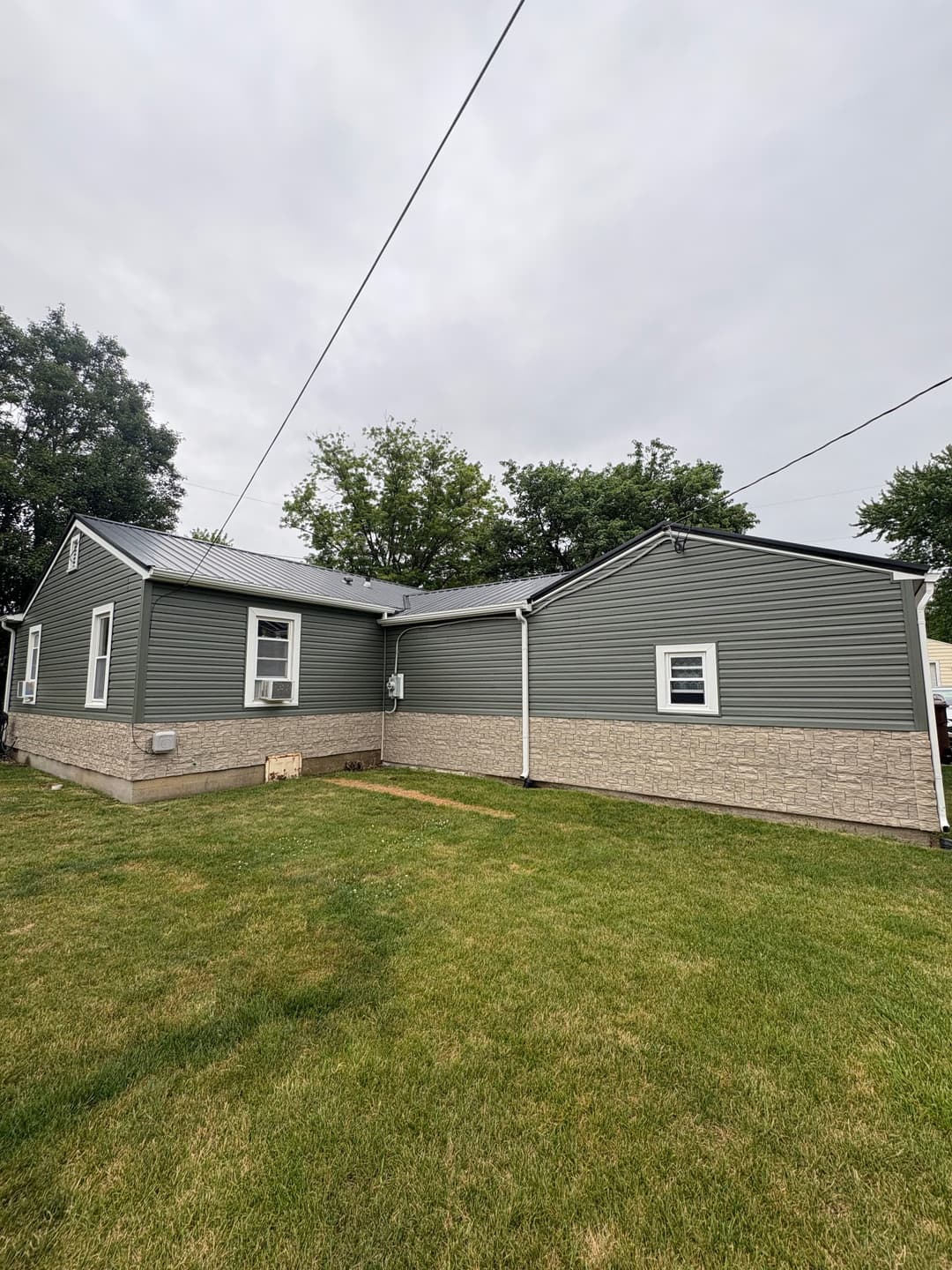Modern gray house with stone foundation, green lawn, and cloudy sky in the background.