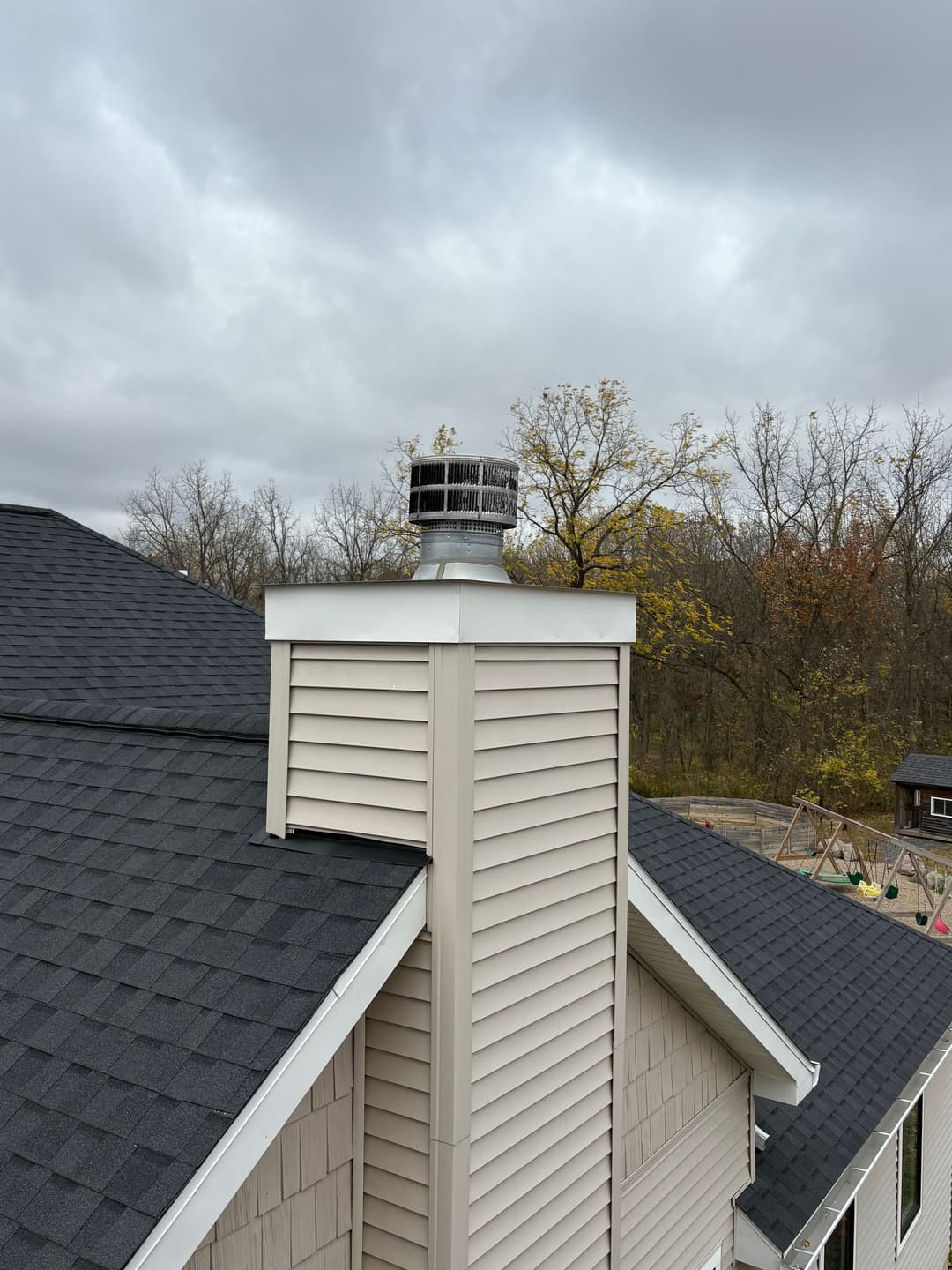 Chimney vent on residential roof with cloudy sky and trees in the background.